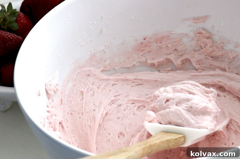 A bowl of creamy, pink Strawberry Buttercream Frosting, ready to adorn freshly baked cupcakes.