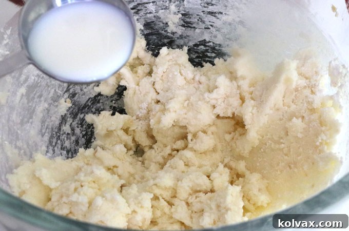 Adding milk gradually to buttercream frosting to achieve the desired creamy texture.
