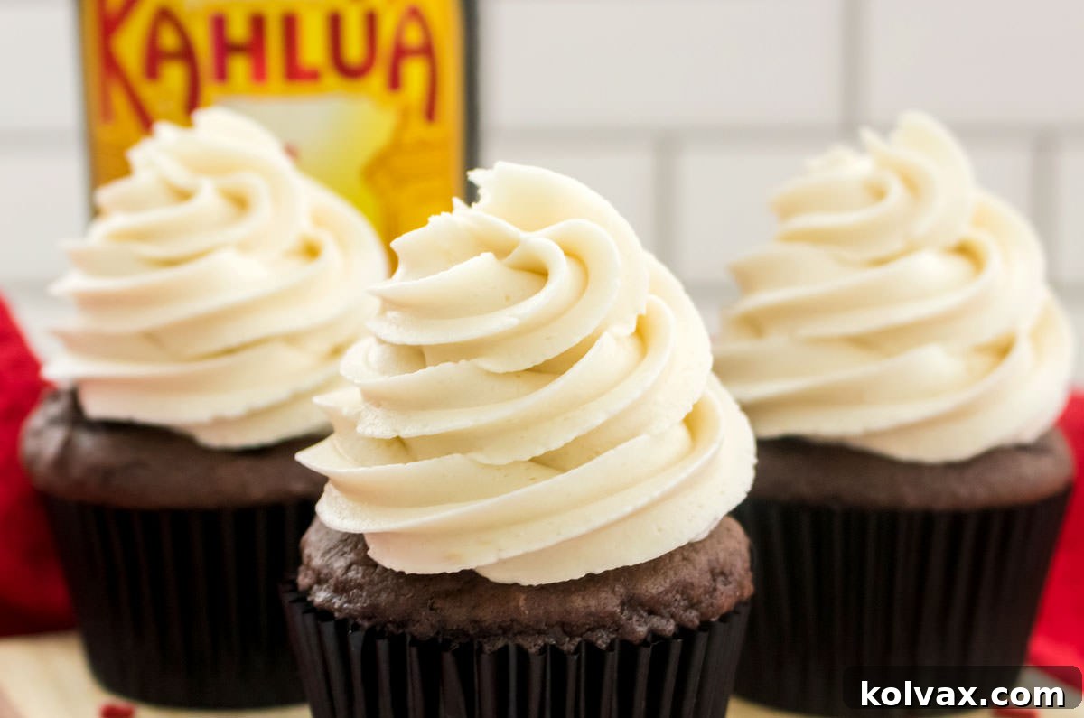 Closeup on three cupcakes topped with Kahlua Buttercream Frosting sitting in front of a bottle of Kahlua Rum and Coffee Liqueur.