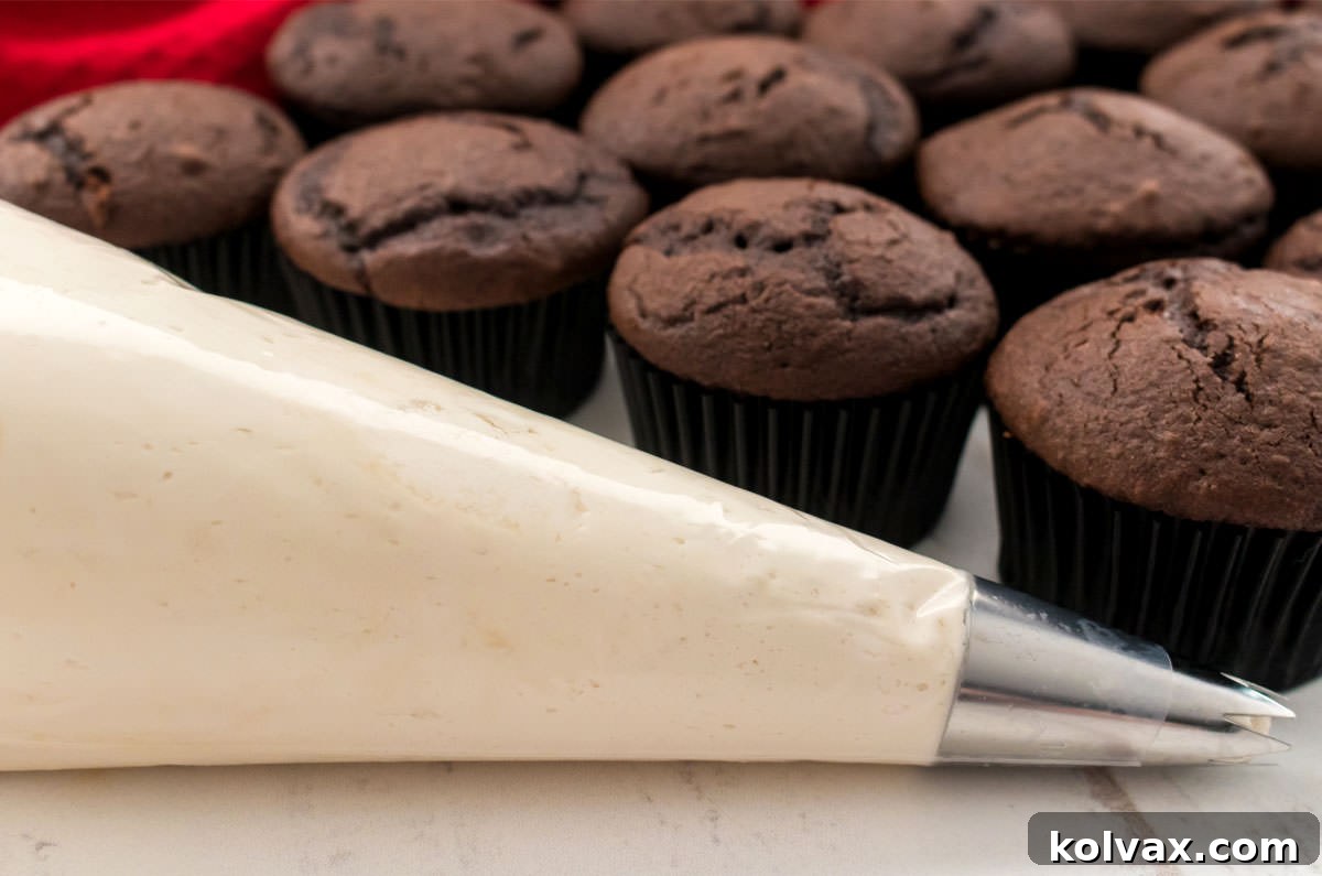 Closeup on a decorating bag filled with Kahlua Buttercream Frosting sitting on a white table with a batch of unfrosted cupcakes.