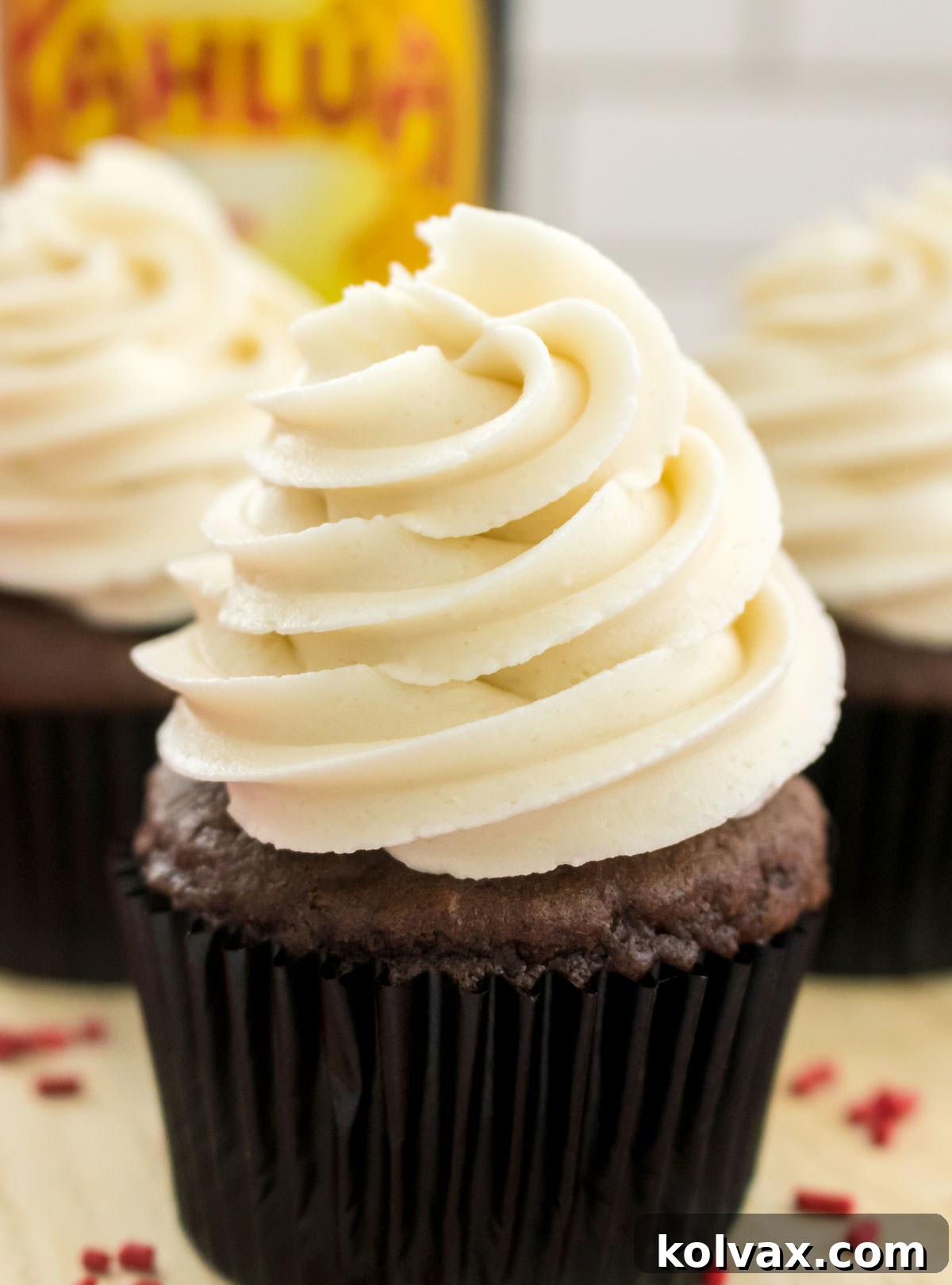 Closeup on a chocolate cupcake frosted with Kahlua Buttercream Frosting sitting on a cutting board in front of a bottle of Kahlua Rum and Coffee Liqueur.