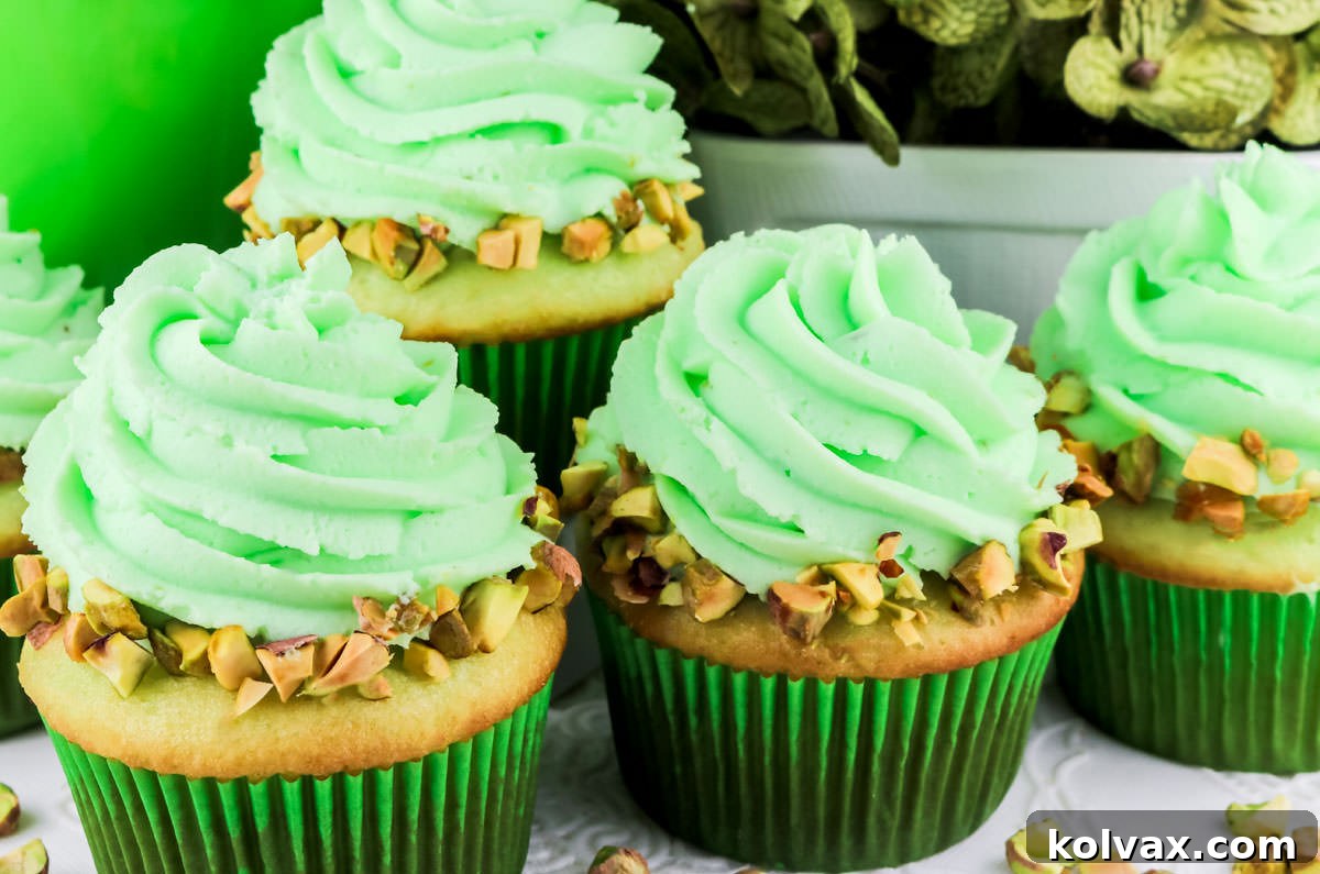 Four Pistachio Cupcakes with Pistachio Whipped Cream Frosting sitting on a white table, ready to be enjoyed.