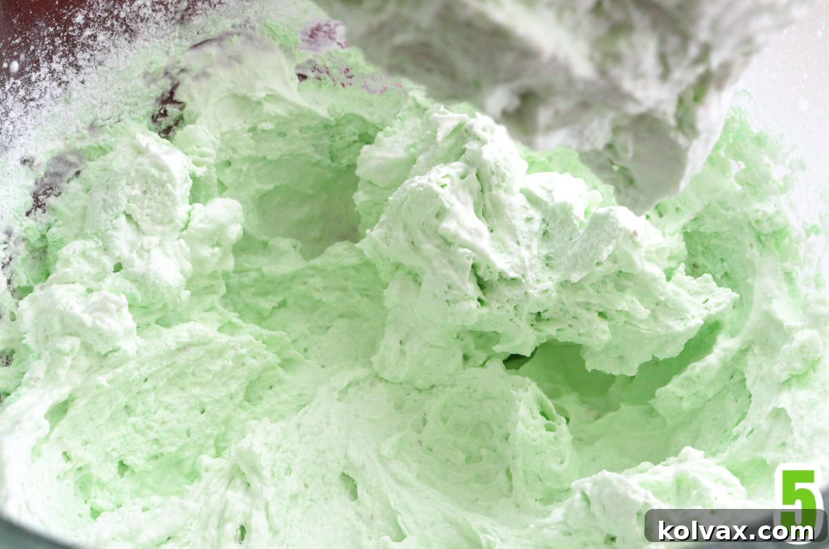 Clear mixing bowl filled with freshly made, light green Pistachio Whipped Cream Frosting, ready to be piped.