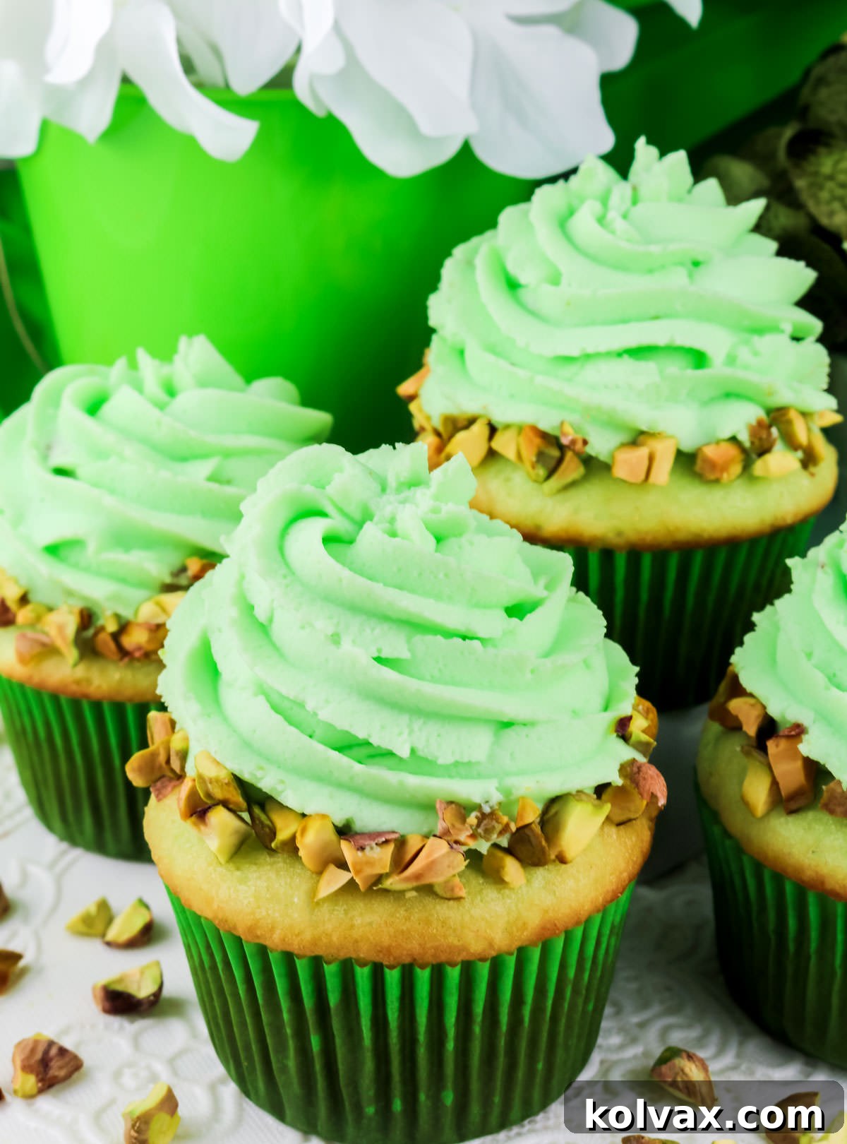 Four beautifully frosted Pistachio Cupcakes with Pistachio Whipped Cream Frosting, garnished with chopped pistachios, on a white table.