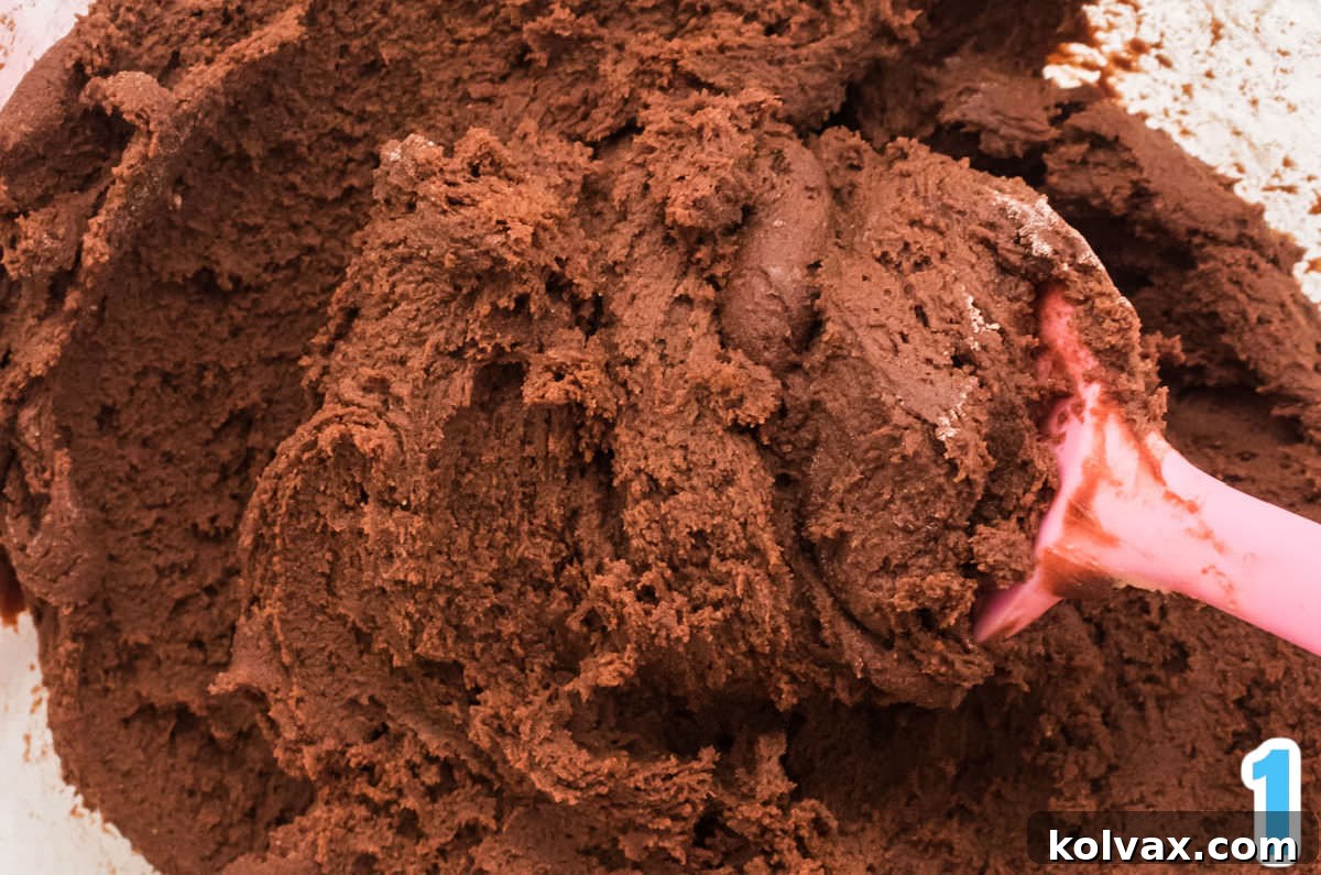 Glass mixing bowl filled with rich, dark chocolate cookie dough, ready for baking into the brownie bar base.