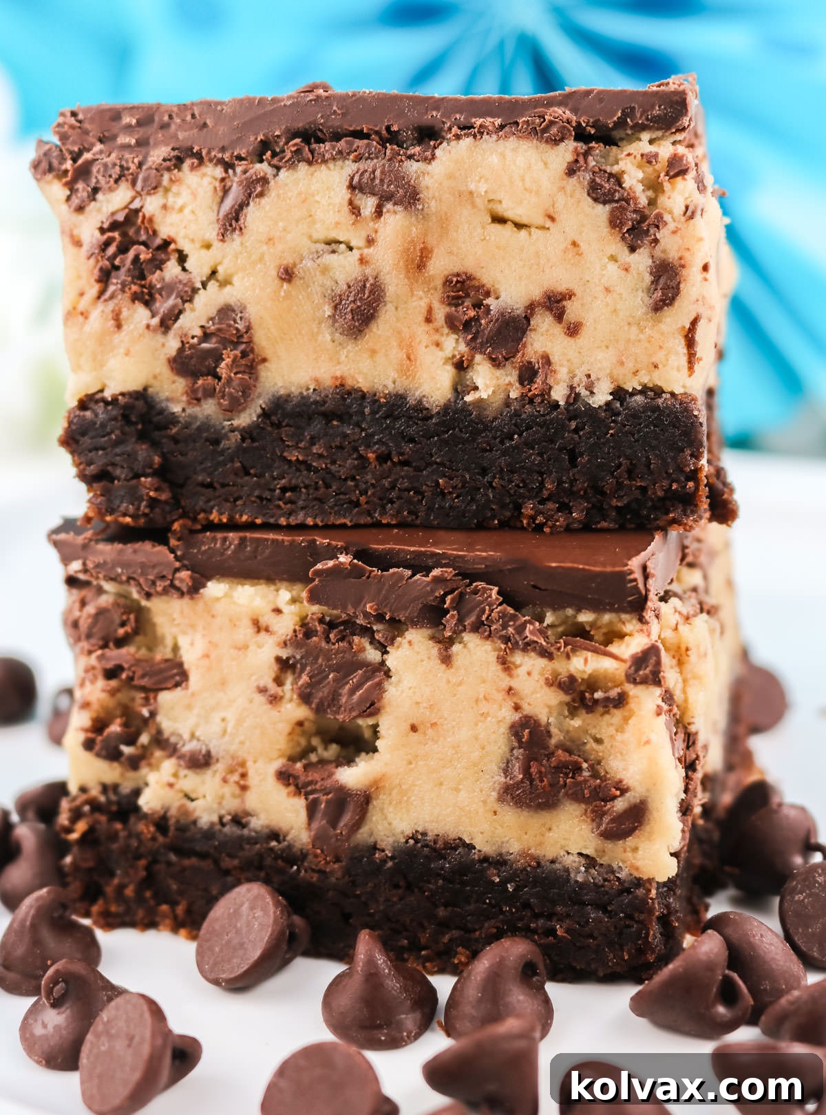 Two perfectly stacked Cookie Dough Brownie Bars on a white plate, surrounded by scattered chocolate chips, highlighting the layers and inviting texture.