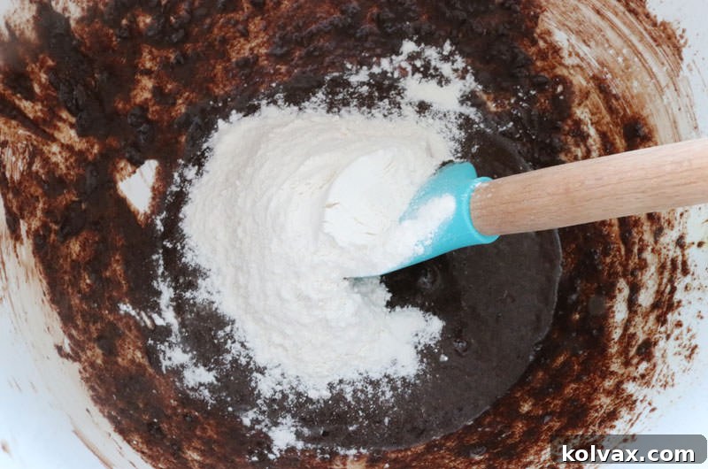 Folding all-purpose flour and baking powder into the brownie batter.