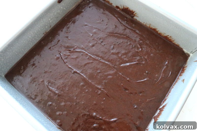 Homemade brownie batter poured into a greased 8x8 inch baking pan, ready for the oven.