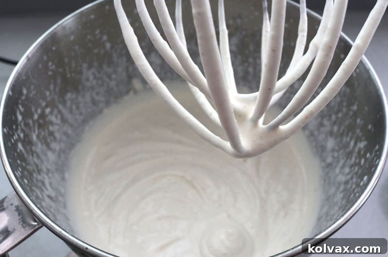 Continuous mixing of the peanut butter whipped cream frosting with an electric mixer, showing the developing thickness and smooth texture as it approaches stiff peaks.