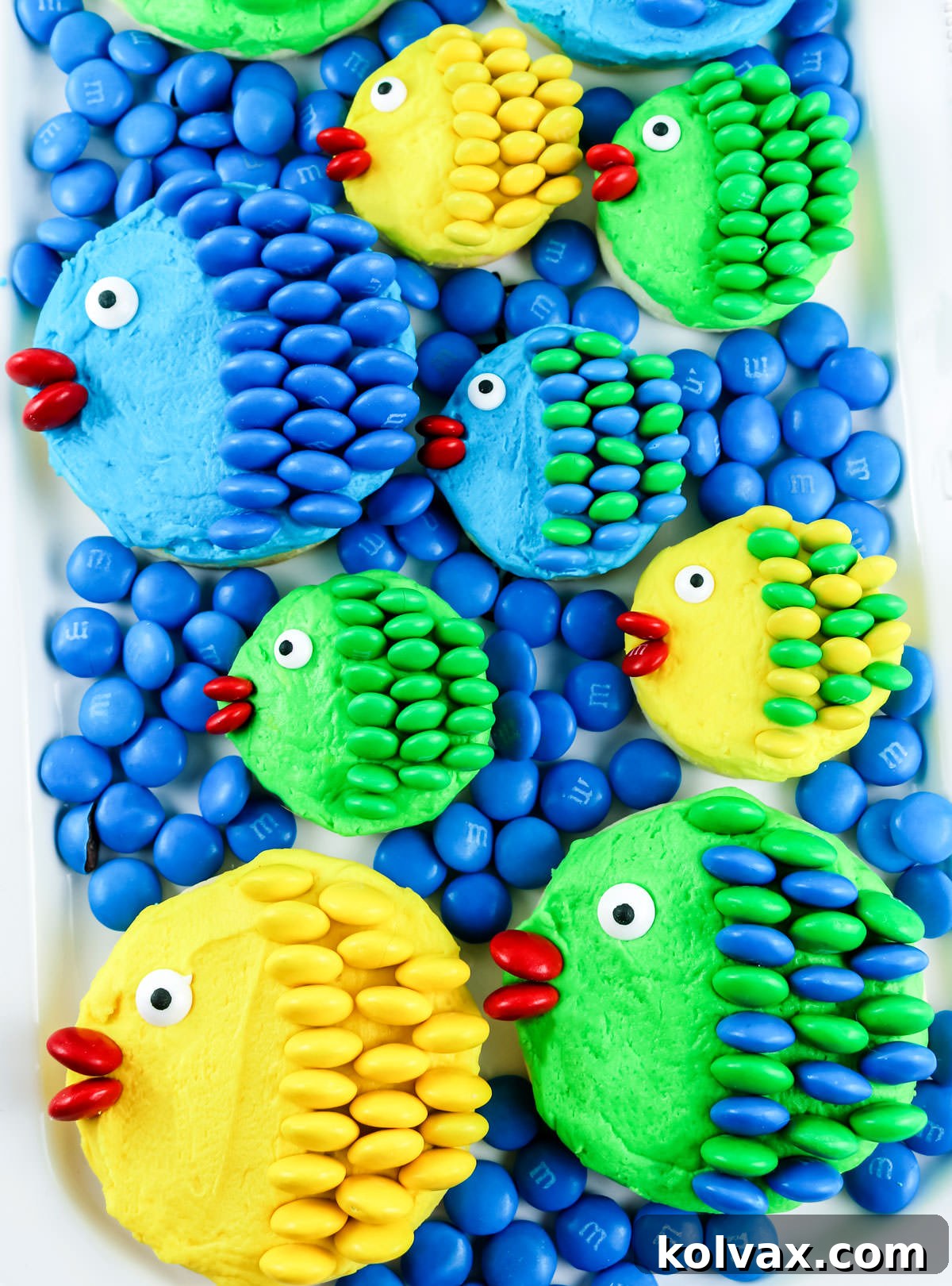 A close-up shot of a white serving platter abundantly covered with various Under the Sea M&M Fish Cookies, artfully surrounded by loose blue M&M's, creating a charming oceanic display.