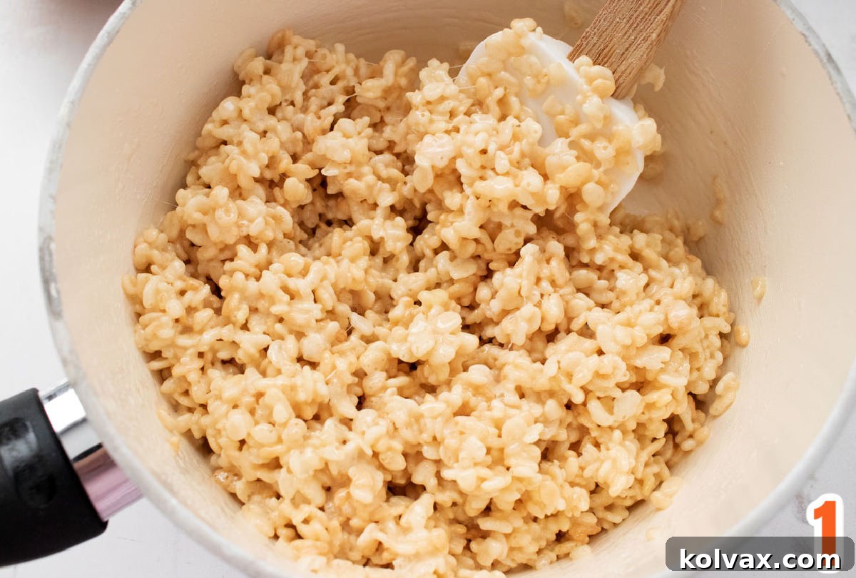 Closeup on a medium saucepan filled with Rice Krispie Treat mixture and a white spoon.