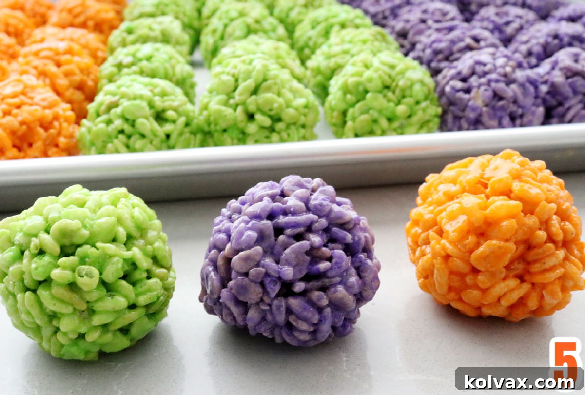 Rows of Halloween Rice Krispie Treat Bites on a cookie sheet with three Green, Purple and Orange Bites in the foreground.