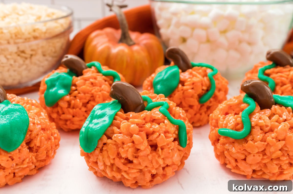Six vibrant orange Pumpkin Rice Krispie Treats arranged on a pristine white table, with bowls of fluffy marshmallows and crispy Rice Krispie cereal subtly blurred in the background, creating a mouth-watering fall scene.