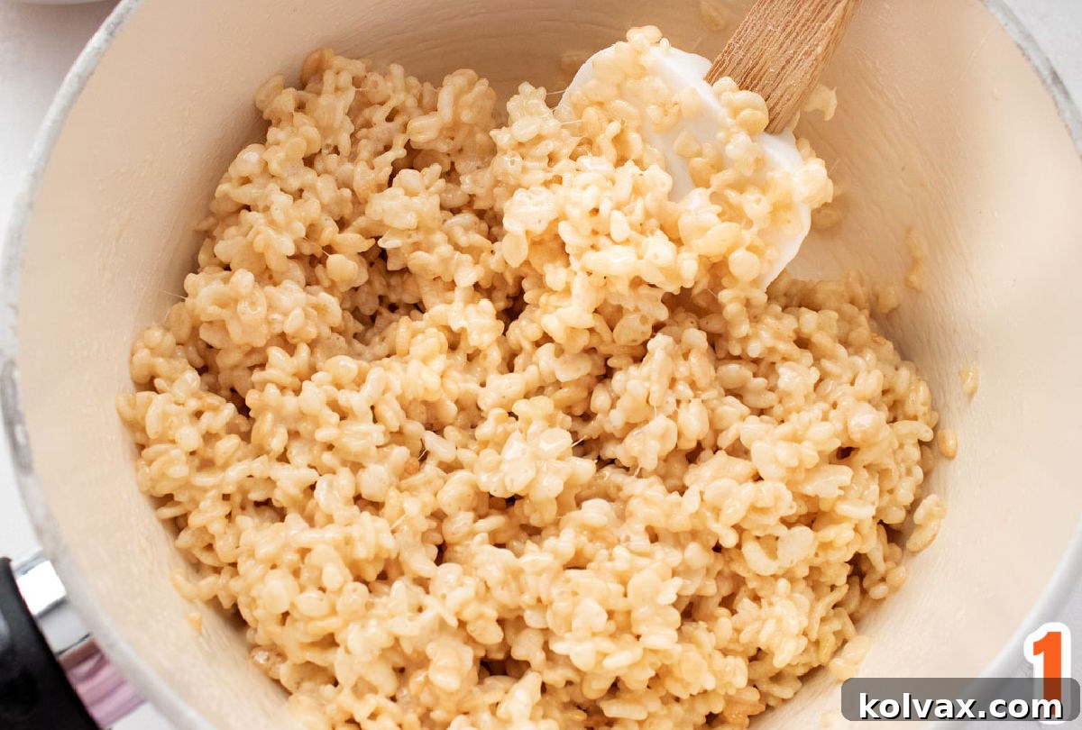 A glistening white saucepan filled with a perfectly warm and gooey Rice Krispie Treat mixture, ready to be shaped and transformed into delicious fall pumpkins. The mixture appears smooth and well-combined, hinting at the perfect texture to come.