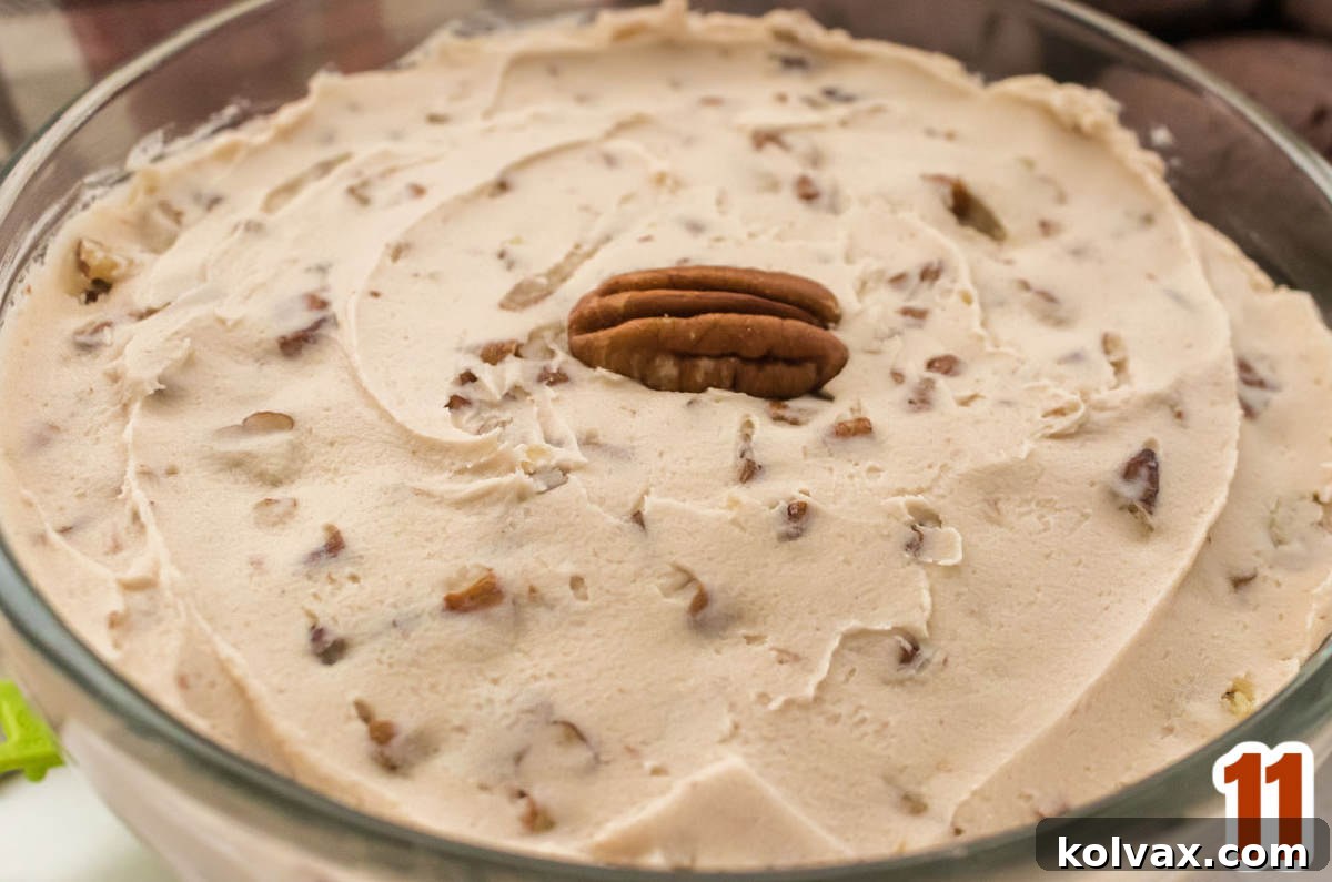 Closeup on a clear glass bowl filled with freshly made homemade Maple Pecan Frosting, showing its creamy texture and visible pecan bits.