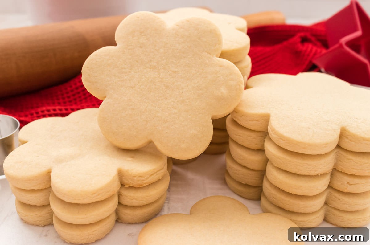 Four neatly arranged stacks of classic sugar cookies, presented on a white table with a rolling pin and a red linen in the background, showcasing their perfect shape.