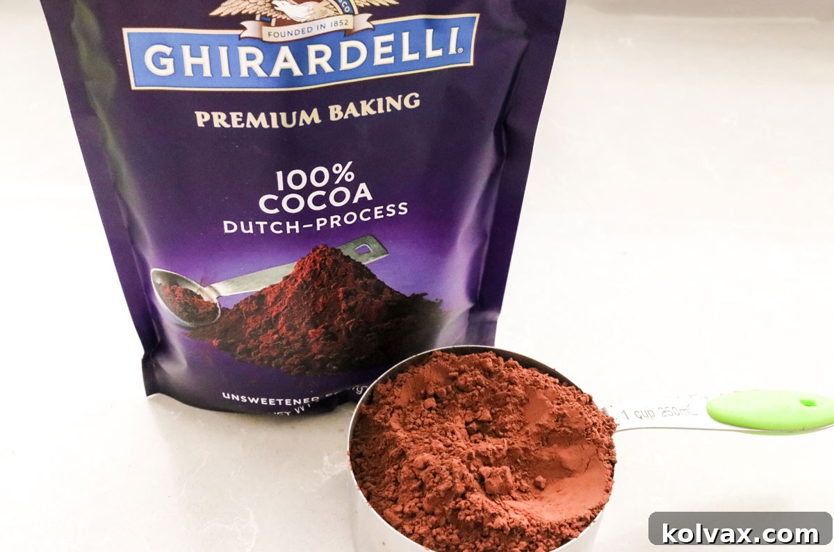 Closeup view of a measuring cup filled with Ghirardelli 100% Dutch Process Cocoa Powder, highlighting its dark, rich color.