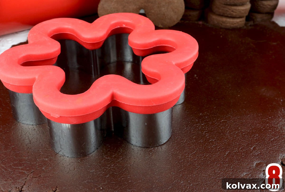 Closeup of chocolate sugar cookie dough rolled out smoothly on a light surface, ready for cutting with a vibrant red flower-shaped cookie cutter.