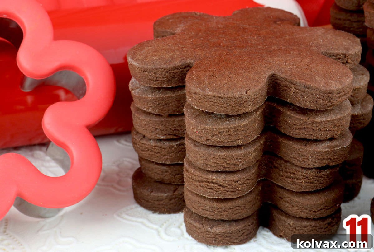 A delightful stack of baked chocolate sugar cookies, alongside a red cookie cutter and a red rolling pin, ready for decorating or enjoying.
