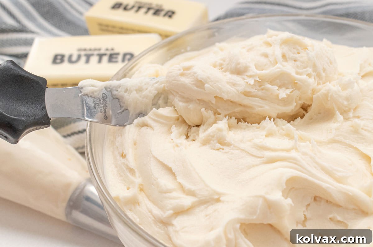 A clear glass bowl brimming with our signature buttercream frosting, accompanied by a spreading knife, sticks of butter, and a piping bag filled with frosting, ready for cookie decoration.
