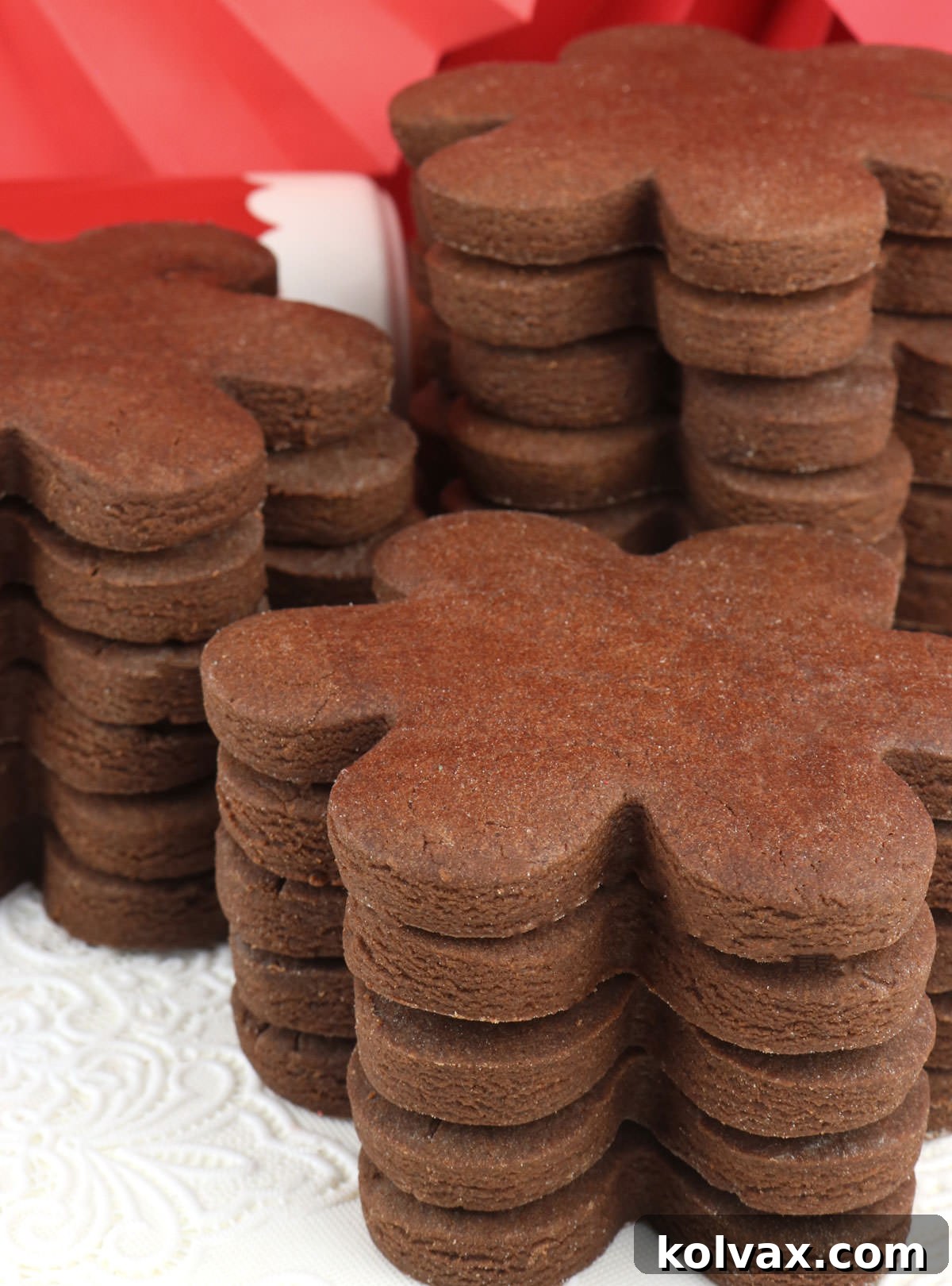 Three perfectly stacked chocolate sugar cookies rest on a white surface, with a red rolling pin visible in the background, symbolizing baking joy.