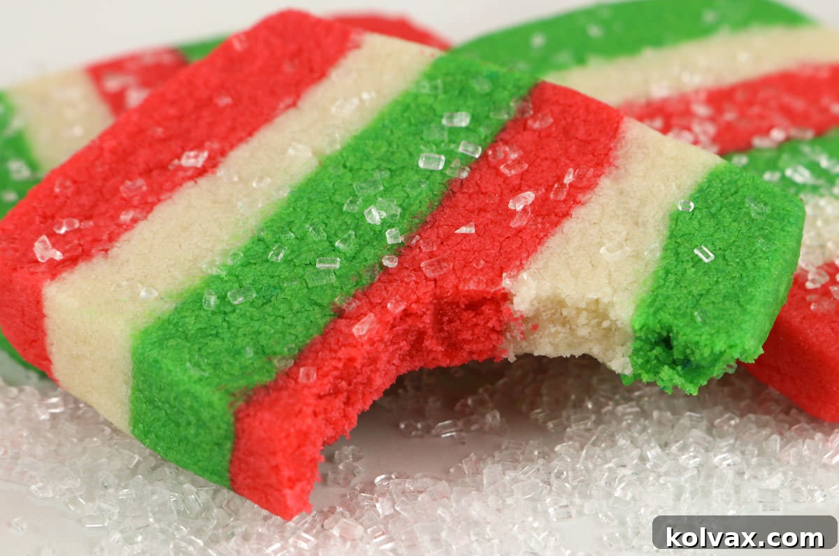 Close up of a Christmas Butter Cookie with a bite taken out of it, showcasing its distinct red, white, and green layers and sparkling sugar topping.