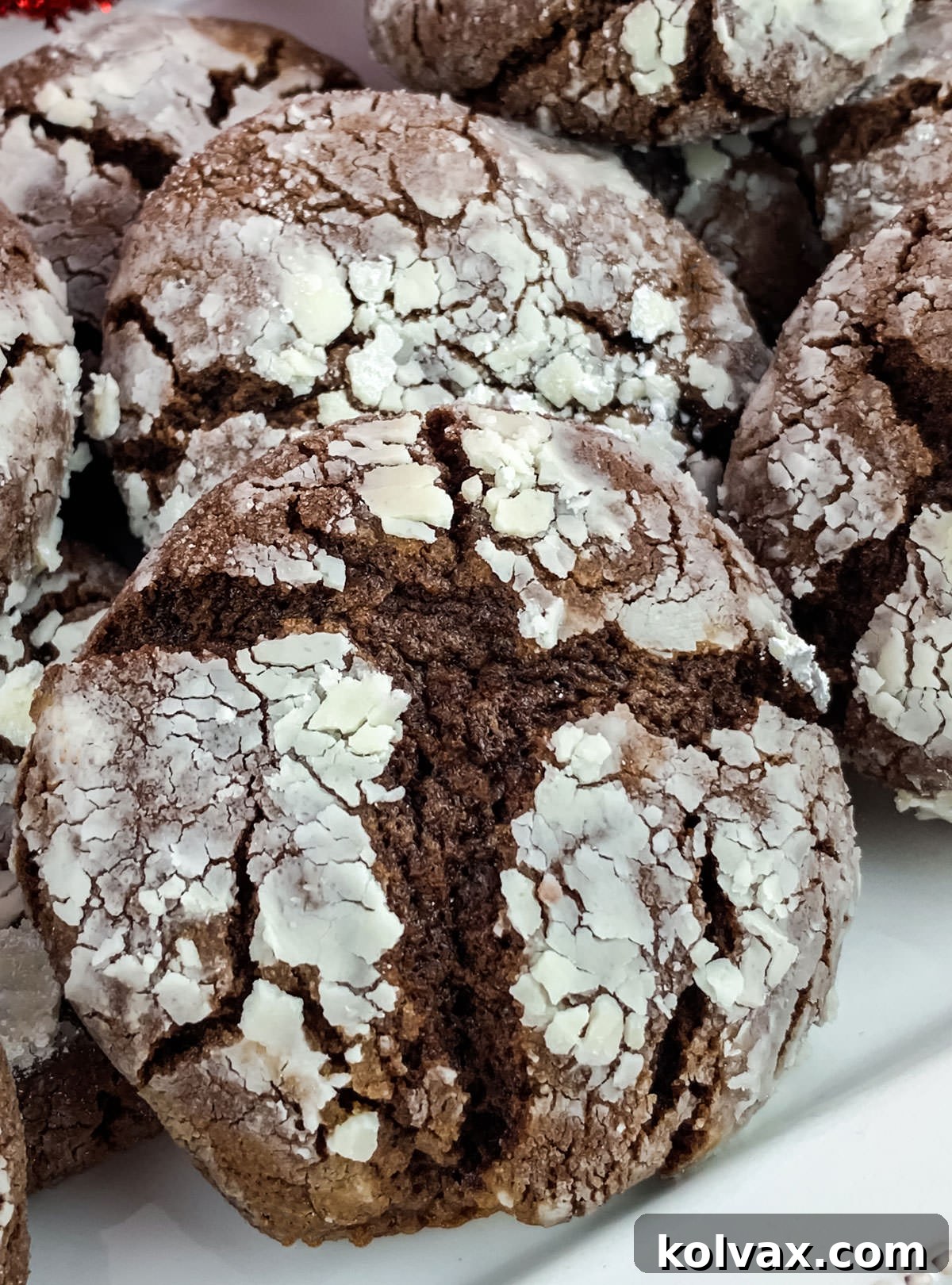 Closeup on a white serving plate abundantly filled with freshly baked Chocolate Crinkle Cookies, showcasing their delightful powdered sugar coating and iconic cracked texture.