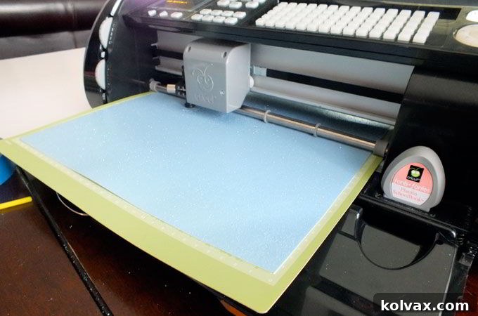 Cutting intricate Happy Birthday signs from blue and white sparkly scrapbook paper using a Cricut, adding a magical touch to the Disney Frozen Centerpieces.