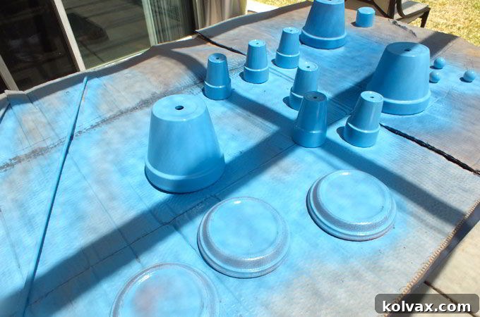 Spray painting terra cotta pots blue for the Disney Frozen Centerpiece base, ensuring a smooth and even coat for your party decorations.