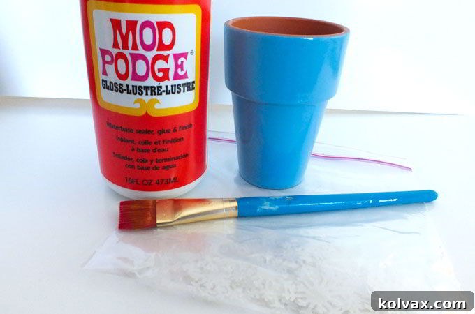 Using Mod Podge to delicately add vellum snowflake embellishments to the painted terra cotta pots for a magical Disney Frozen Centerpiece.