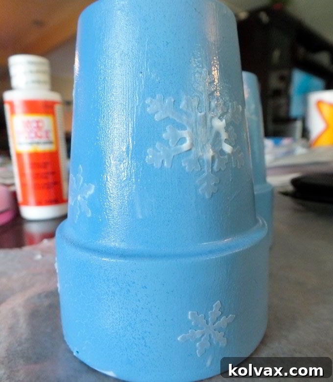 Applying handcrafted vellum snowflakes to the freshly painted terra cotta pots, sealing them with Mod Podge for a durable and magical Disney Frozen Centerpiece.