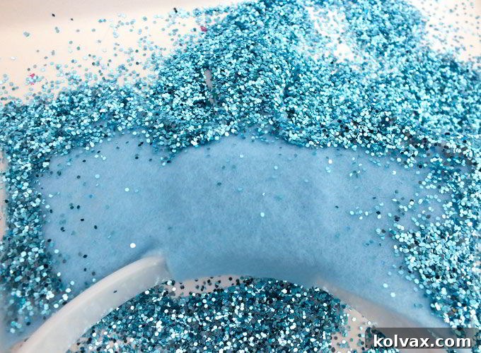 Liberally sprinkling blue glitter onto the glue-coated edges of the Elsa Crown.