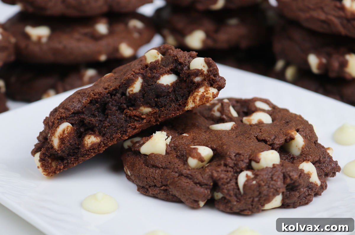 Two soft Chocolate White Chocolate Chip Cookies, one broken in half to show its fudgy interior and melted white chocolate, resting on a white plate surrounded by loose white chocolate chips.