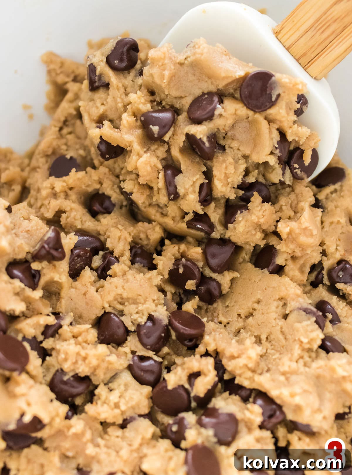 Nutty Brown Butter Chocolate Chip Perfection 4 Closeup on a white mixing bowl filled with rich brown butter chocolate chip cookie dough, alongside a wooden spatula, ready for baking.