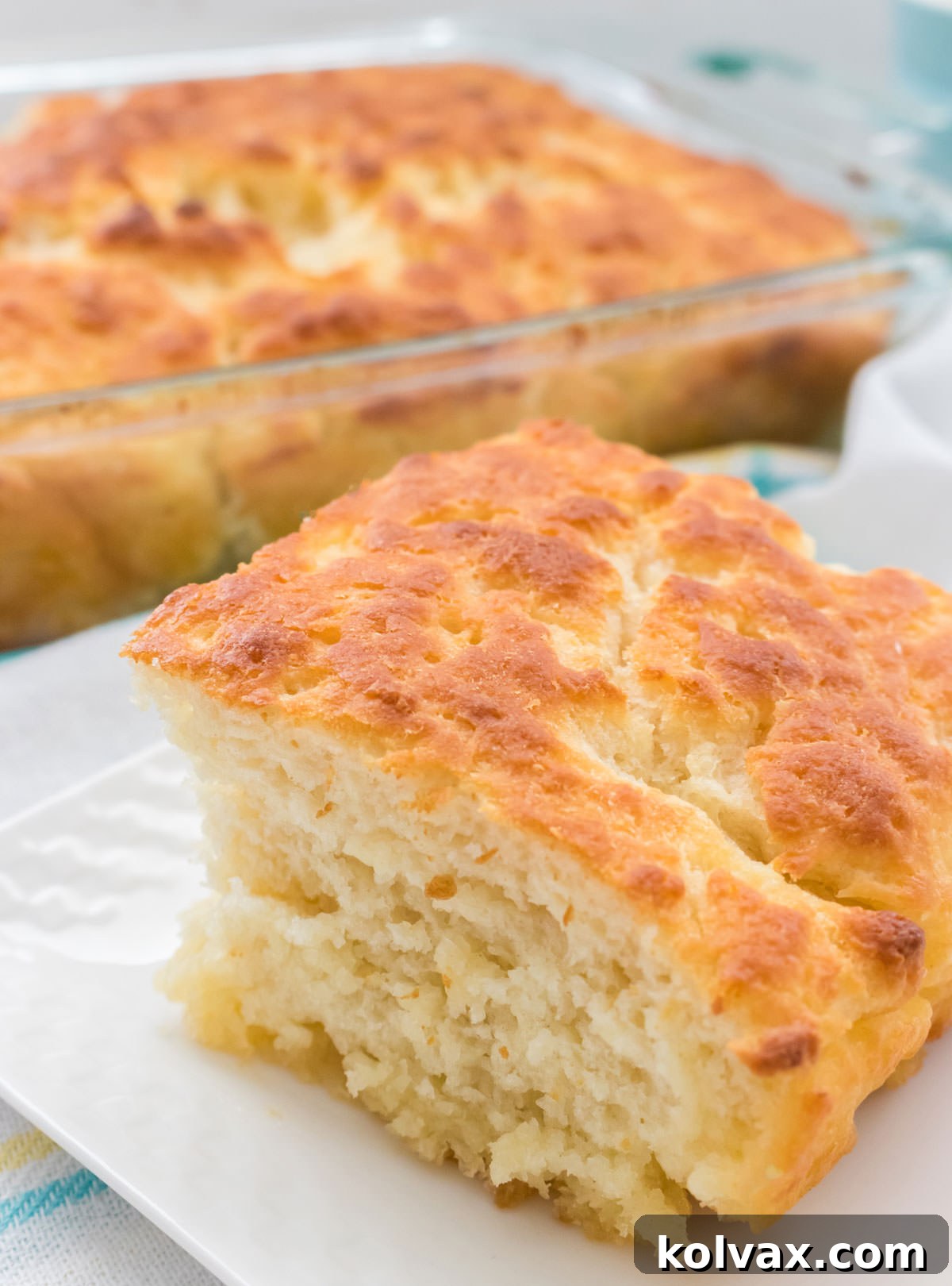 Melt-in-Your-Mouth Buttery Biscuits 6 Closeup of a single Butter Swim Biscuit served on a white plate, with the pan of still-warm Butter Dip Biscuits blurred in the background.