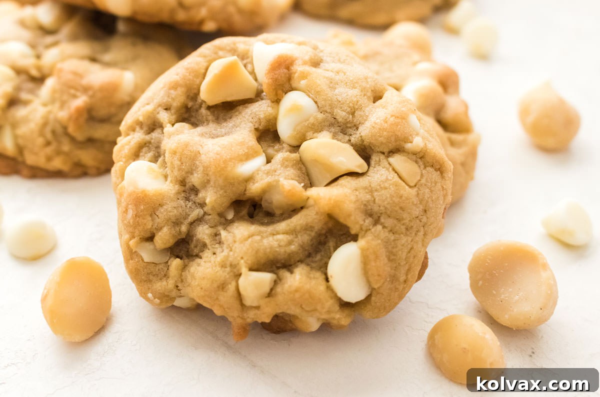 Closeup on a White Chocolate Macadamia Nut Cookie sitting on a white table surrounded by White Chocolate Chips.