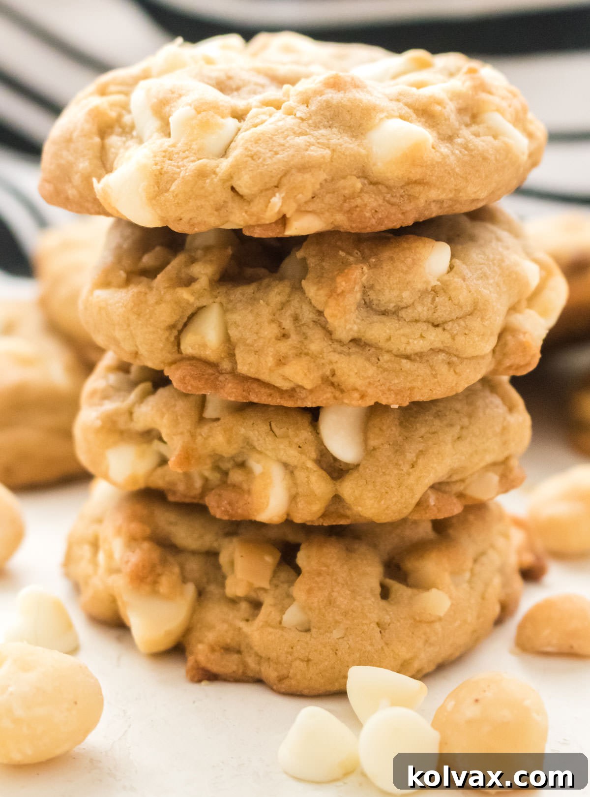 Closeup on a stack of White Chocolate Macadamia Nut Cookies sitting on a white table surrounded by White Chocolate Chips.
