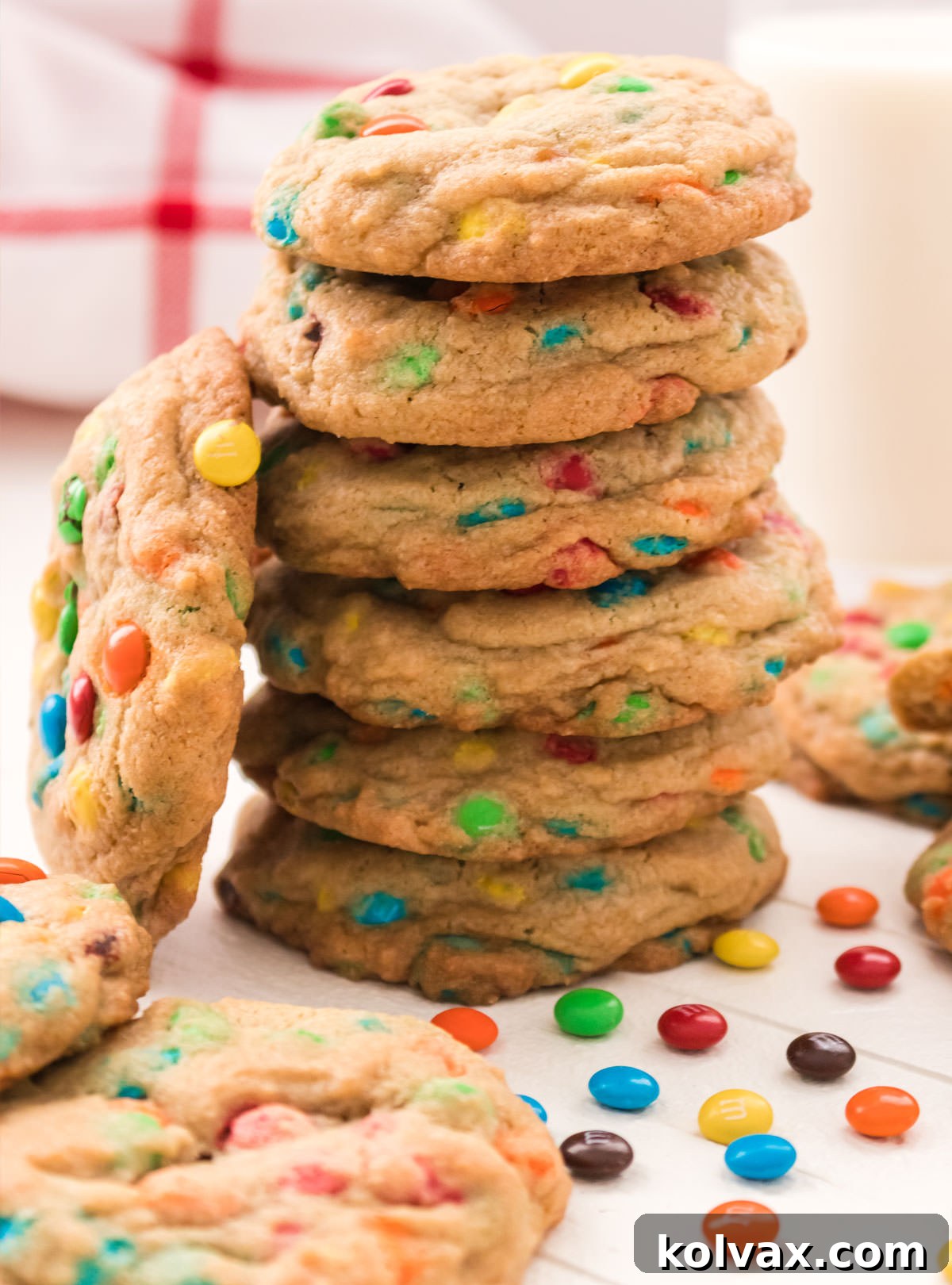 A beautiful close-up of a stack of six perfectly baked Mini M&M Cookies, nestled on a white table. Loose M&M Minis are scattered around, emphasizing the colorful and delicious nature of the cookies.