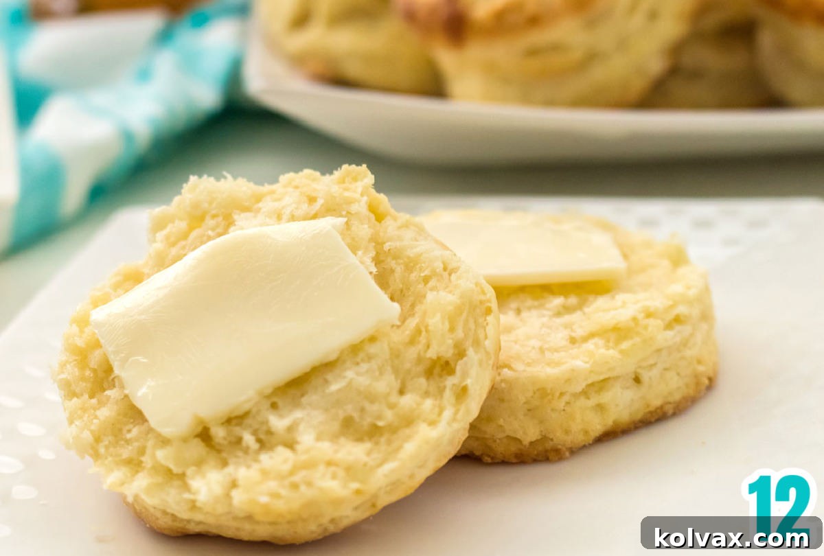 Closeup on a small white plate with a warm, fluffy Buttermilk Biscuit that has been cut in half, revealing its tender layers and a melting pat of butter inside.