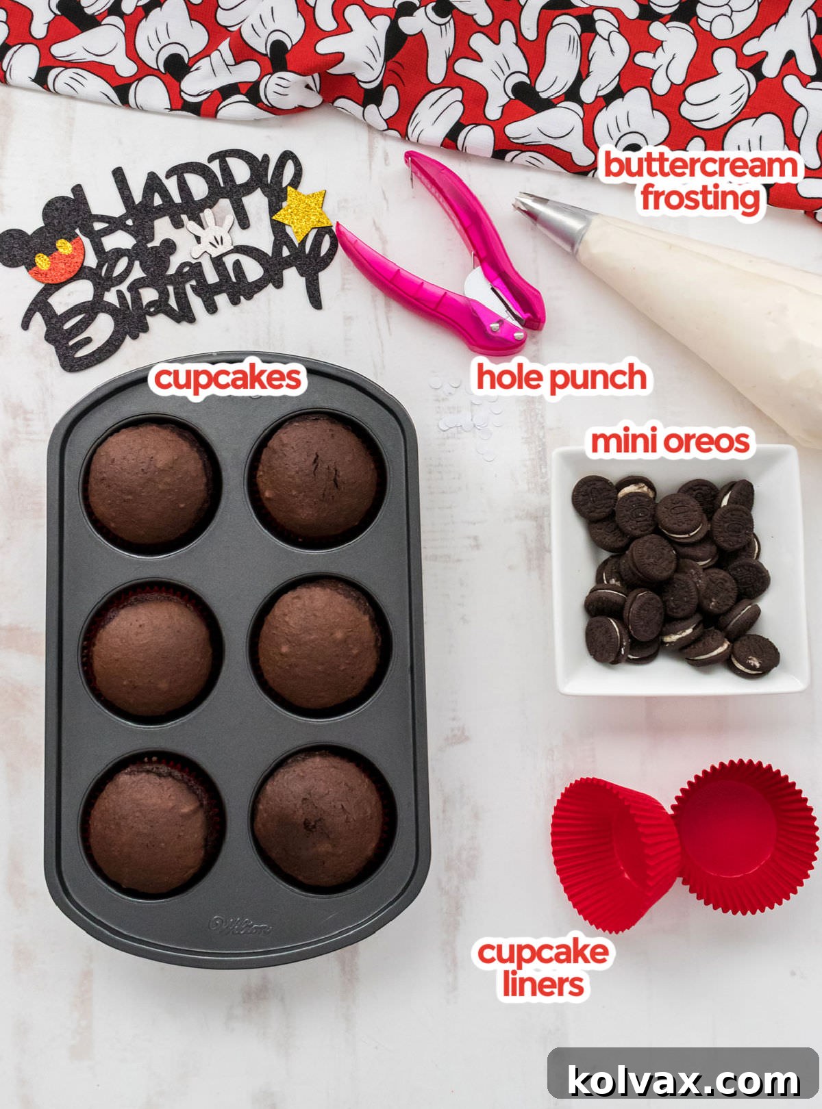 All the essential ingredients for Mickey Mouse Cupcakes laid out: chocolate cupcakes, buttercream frosting, mini Oreos, red liners, and a hole punch.