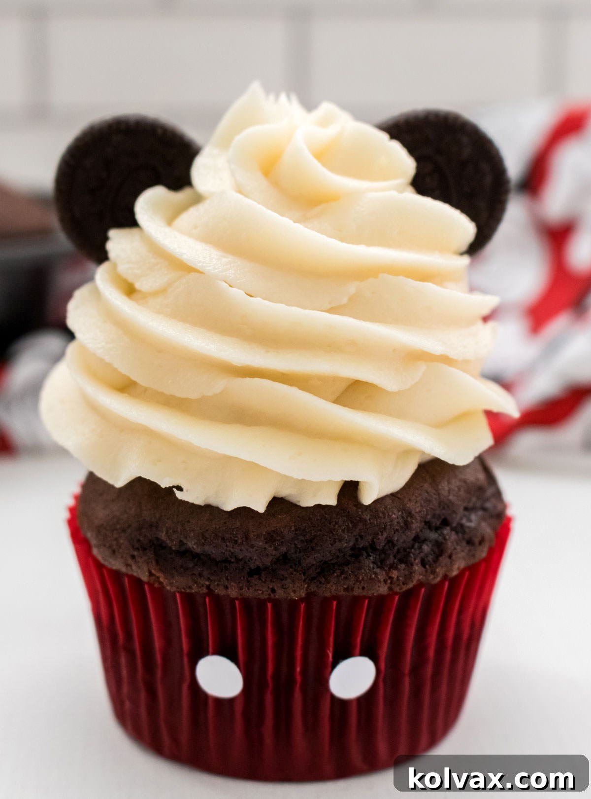 A closeup of a finished Mickey Mouse Cupcake, showing its detailed frosting, Oreo ears, and buttoned red liner, against a whimsical Disney backdrop.