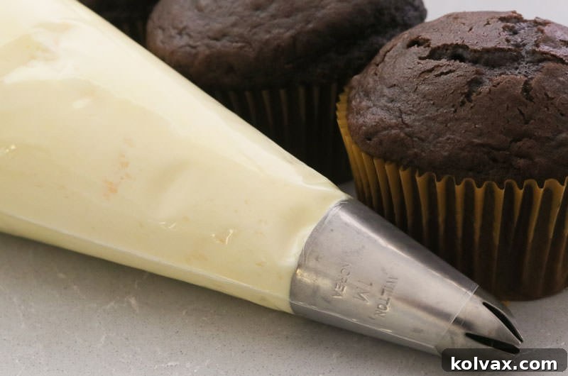 Freshly frosted cupcakes and a piping bag filled with Banana Whipped Cream Frosting, showcasing its perfect consistency
