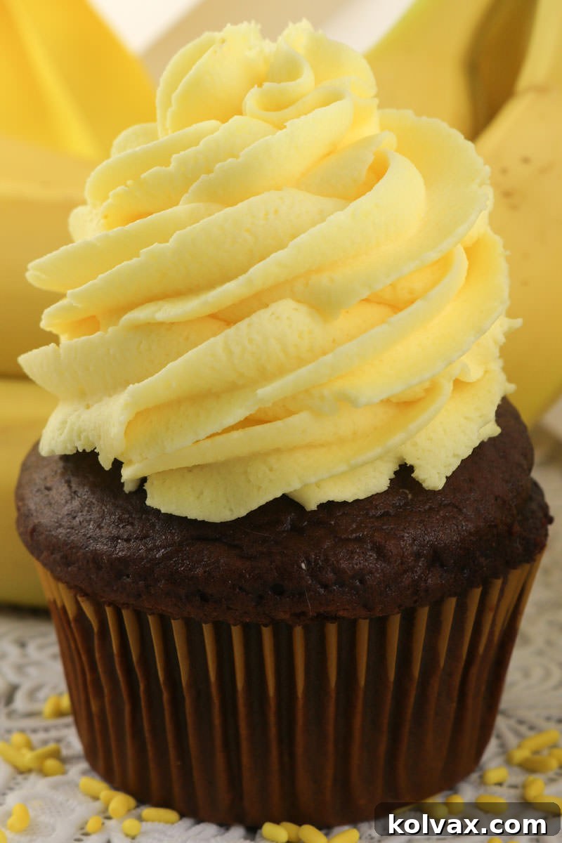 A tall, elegant swirl of Banana Whipped Cream Frosting on a cupcake, garnished with a sliced banana