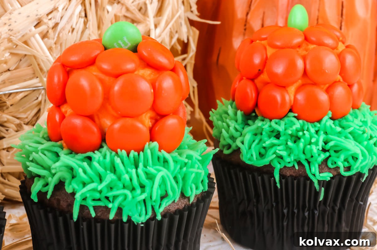 Closeup on two Pumpkin Patch Cupcakes sitting in front of a mini bale of hay and a pumpkin decoration, showcasing their adorable design.