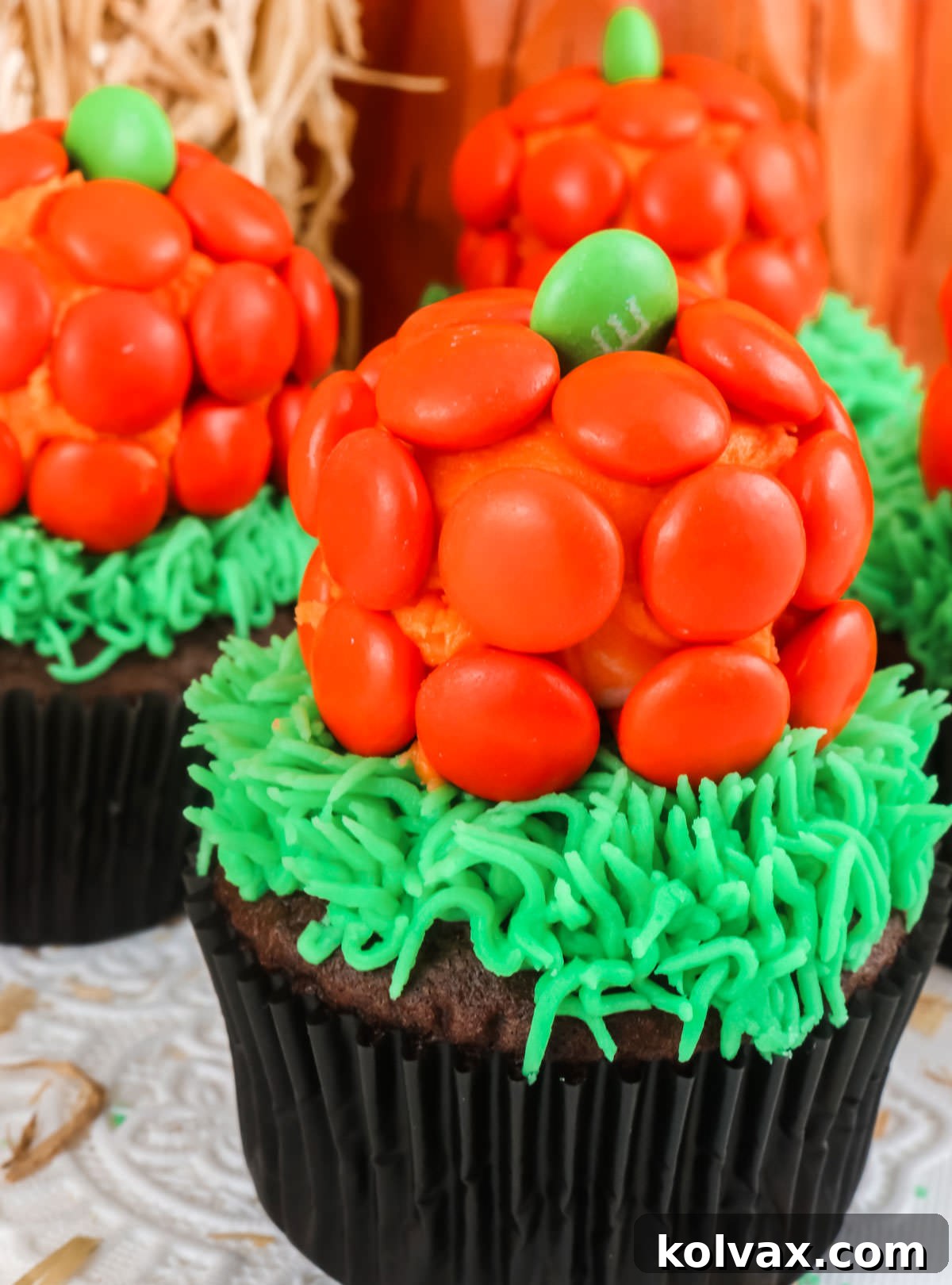 Closeup on three finished Pumpkin Patch Cupcakes sitting on a white table, adorned with festive Halloween Decorations in the background.