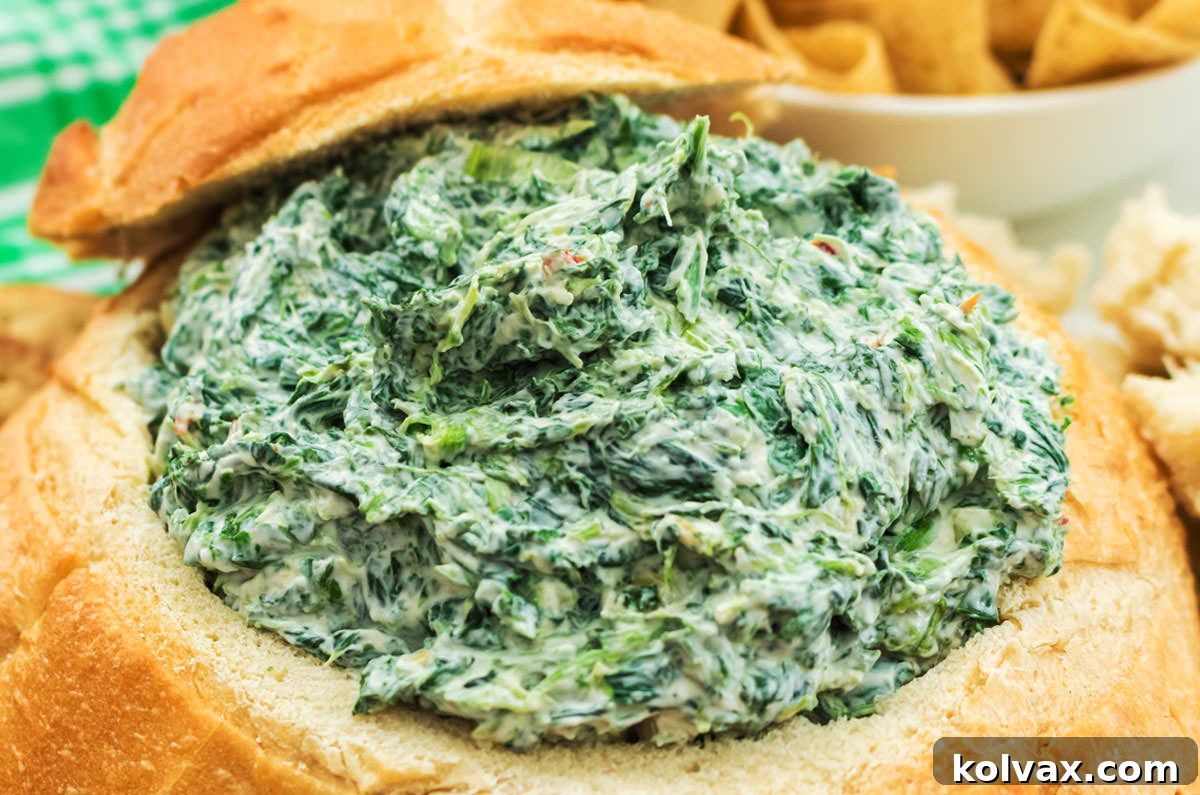 Close up of Creamy Spinach Dip served in a hollowed out Sourdough Round, surrounded by chips and bread pieces. A perfect party appetizer.