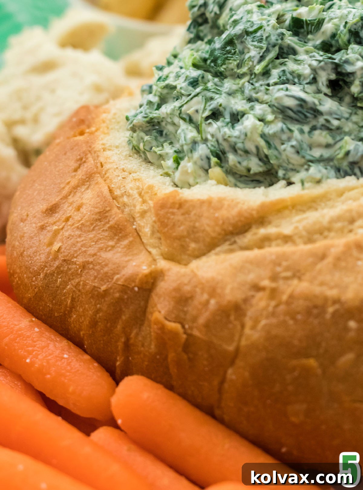 Closeup on a Sourdough round filled with Creamy Spinach Dip and surrounded by carrot sticks and pieces of sourdough bread.