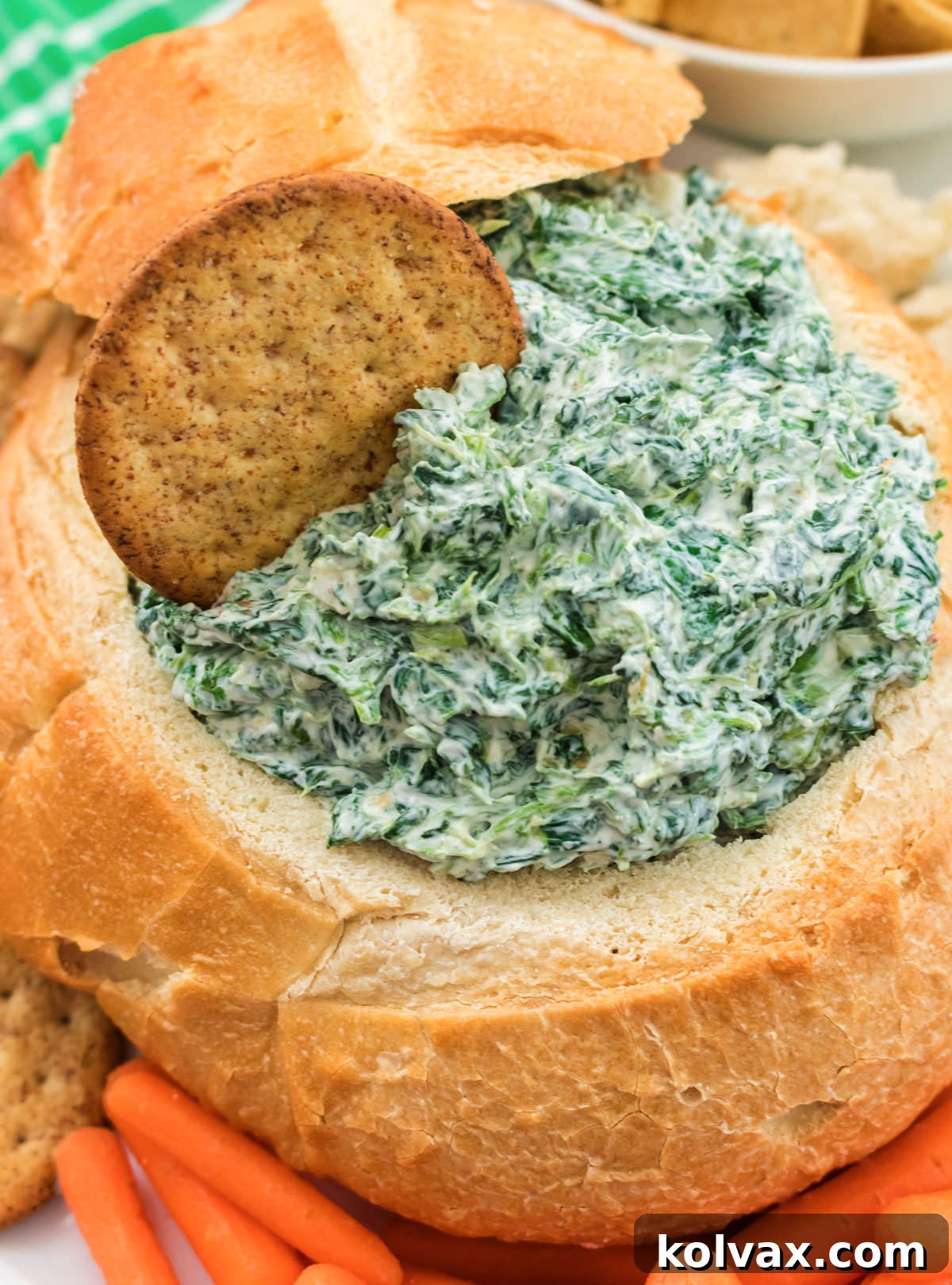 Closeup on a batch of Creamy Spinach Dip in a hollowed out loaf of sourdough bread surrounded by carrots, crackers and pieces of bread, ready for serving.