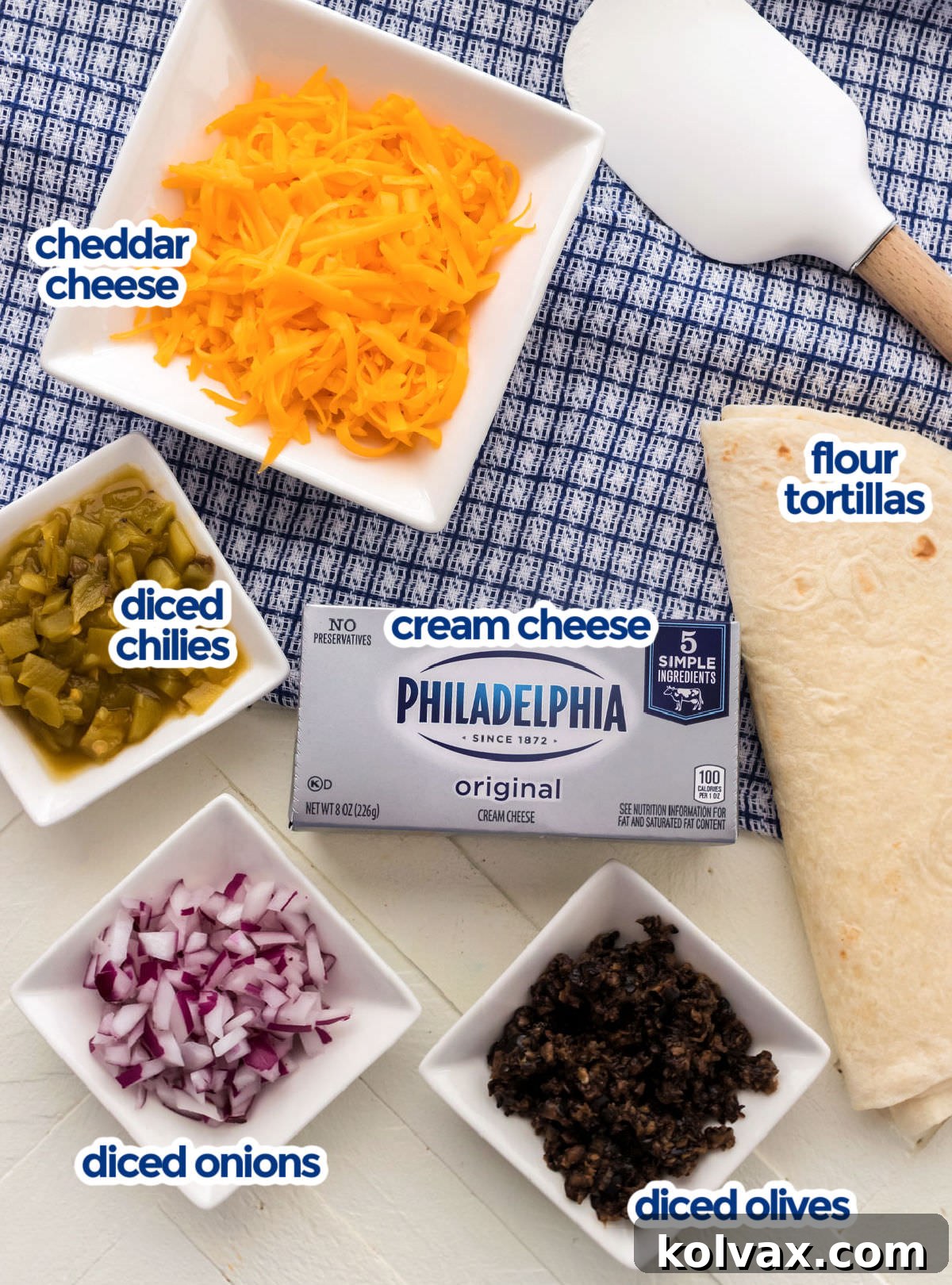 All the ingredients needed to make Tortilla Pinwheels, neatly arranged: cream cheese, shredded cheese, flour tortillas, diced green chilies, chopped red onion, and sliced olives.