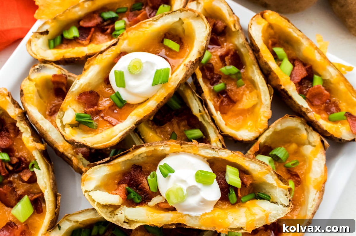 Crispy Loaded Potato Boats 2 Closeup on a stack of golden brown Potato Skins overflowing with melted cheese and crispy bacon bits, garnished with fresh green onions, sitting on a white serving platter.